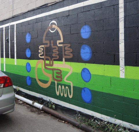 partially finished mural on black background in an alley, green stripes near the bottom, blue circles beside brown squiggles, milk x weed
