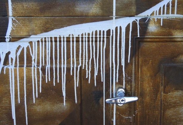 white drips of paint on a wood garage door, metal door handle 