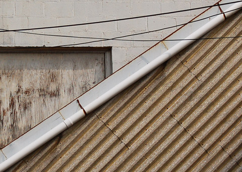 corrugated plastic panels on angle in front of concrete block wall with window covered with plywood 