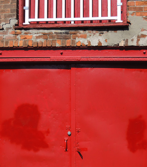 part of a bright red double metal door in a brick building 