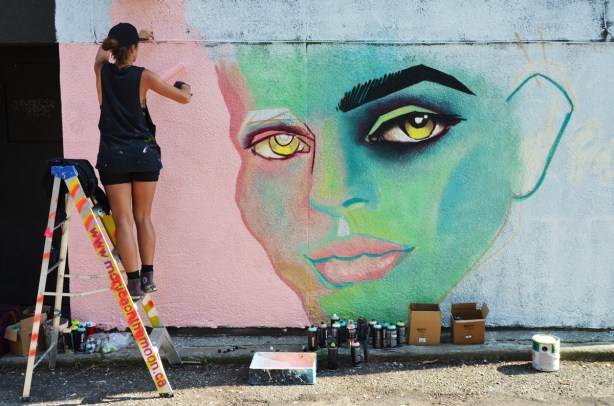 woman rolling paint to make pink background on a mural