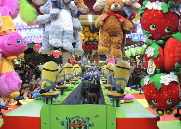 woman running a game at the CNE, she is surrounded by prizes such as stuffed minions and other animals