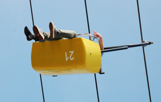 from below, two people riding on the Skyride, an arm hangs over the side, and there appear to be only three feet 