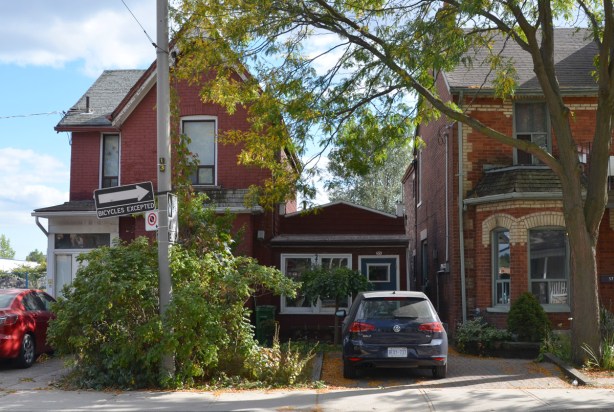 a car is parked in front of a very small one storey house that is between two large and taller houses, 