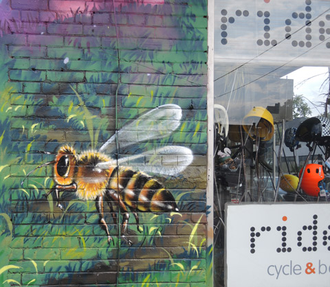 part of a larger mural by Clandestinos (Shalak Attack and Bruno Smoky) on the side of Riders bike store, a large bumble bee by the front window