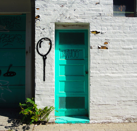 a bright turquoise door in a building that has been painted white - some of the old brick shows throw the peeling paint. 