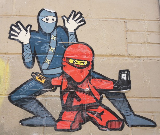 urban ninja squadron man with planet_selfie character in red with red helmet, pasteup on a wall 