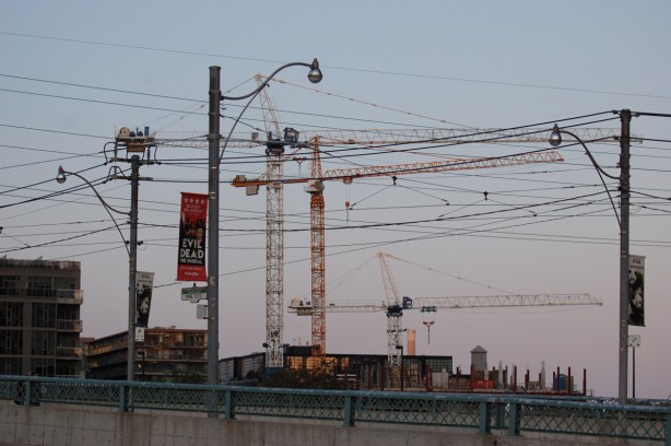 evening light, cityscape with many construction cranes, light poles and utility poles and wires, evening, 