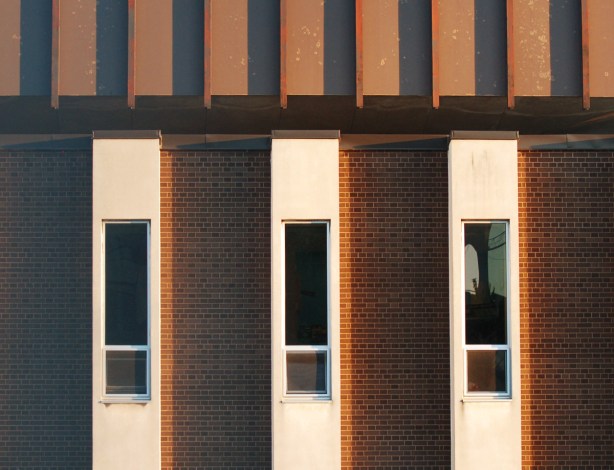part of a wall, vertical stripes of brick sections and white sections, narrow windows in the white sections, 3 windows in total 