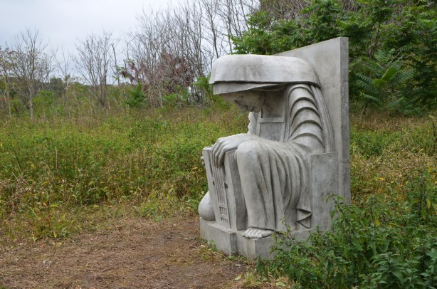cast concrete sculpture of a seated woman with her head bent forward 