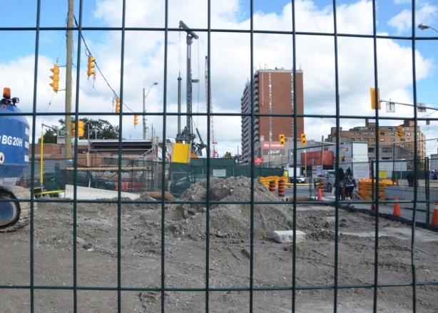 wire fence in front of a construction site, lots of dirt, street and buildings in the background. 