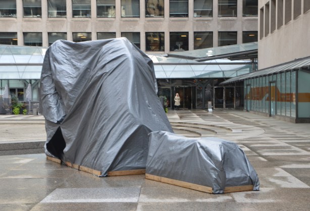 a sculpture in a public square is covered by grey plastic 