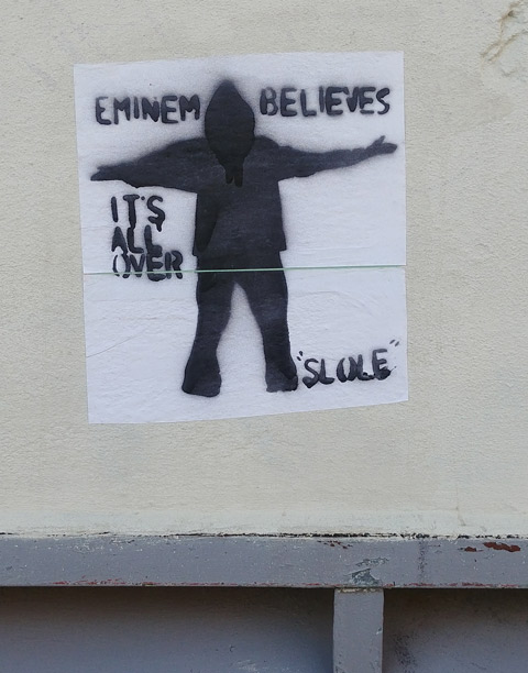 stencil, black on white, pasteup, black man in silhouette with his arms out, with words that say Enimem believes it's all over, slole 