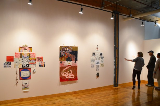 three people in an art gallery looking at drawings by sab meynert.