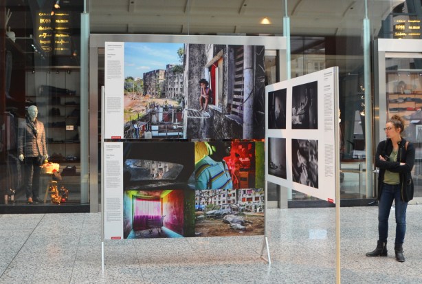 display of photos in front of a store with a male mannequin dressed for fall, also a woman on the other side looking at the pictures 