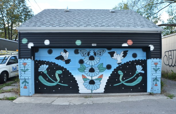 mural on an alley garage, black and blue predominant colours, some flowers, and birds 