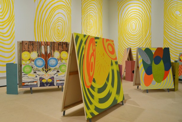 artwork by sandra Meigs at the Art Gallery of Ontario, paintings back to back, standing on the floor, bright colours, banners hanging on the walls of concentric yellow circles on white