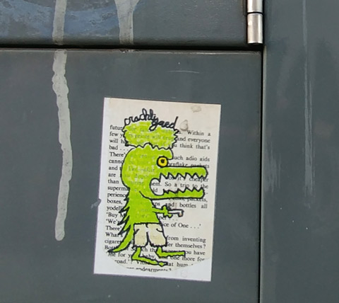 a sticker on the side of a grey metal box, a green alligator like character, walking on two legs, with a green head on top (two heads), drawn on white background that had words printed on it. 