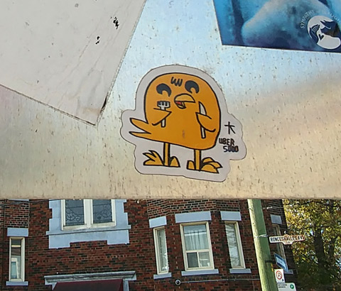 an uber 5000 yellow birdie sticker on the back of a street sign, he's holding a knife and fork 