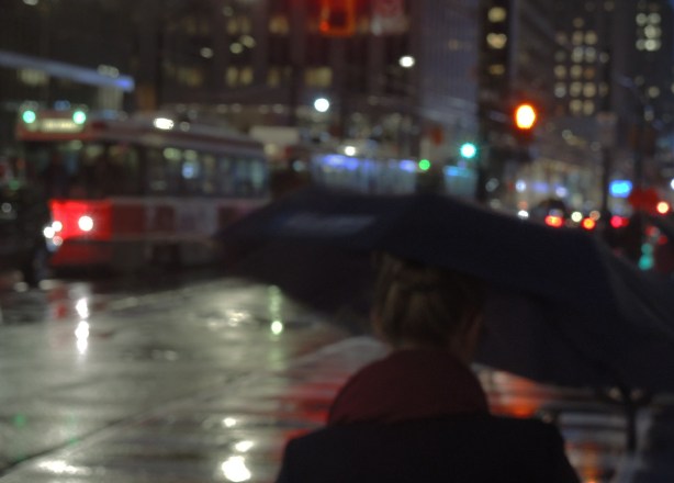 woman with umbrella in the foreground, traffic on a rainy night in the background