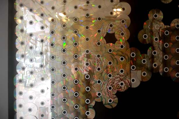 design and pattern made with many old CD's mounted on a wall inside the window of an empty store. 
