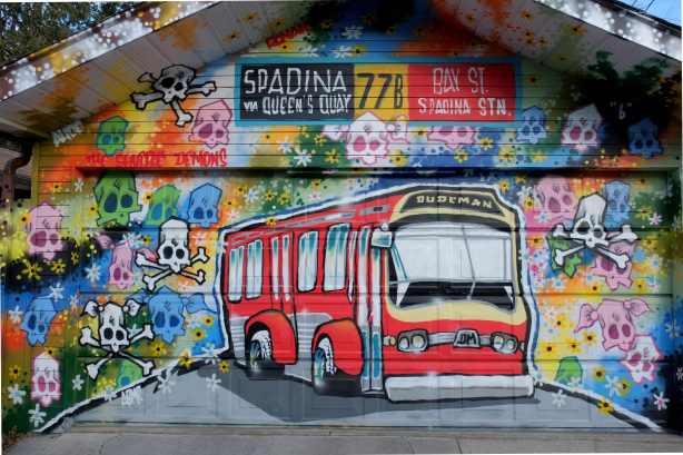 a mural by dudeman, TTX bus, spadina sign, and lots of different coloured skulls