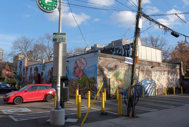 corner where two alleys meet, a green P parking lot and a building with murals on two sides. 