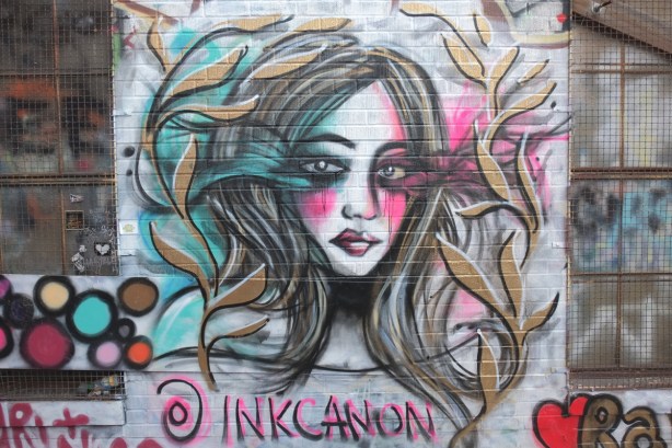 street art painting by inkcanon of a woman with long hair, vines growing up on either side of her. 