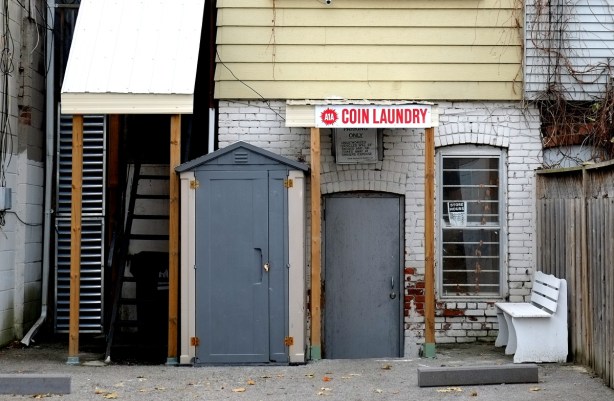 lane entrance to a coin laundry, two grey doors, white bench outside the doors. 