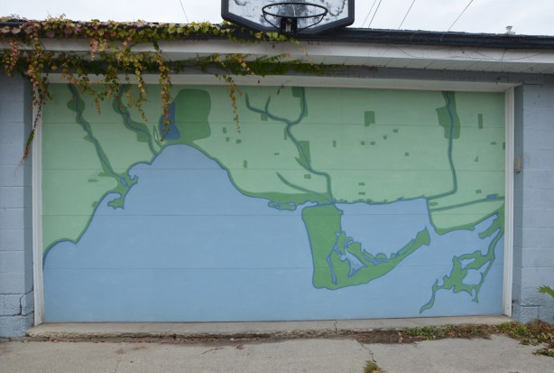 basketball hoop above a garage door that has a large map of Toronto, in blue and green painted on it. 