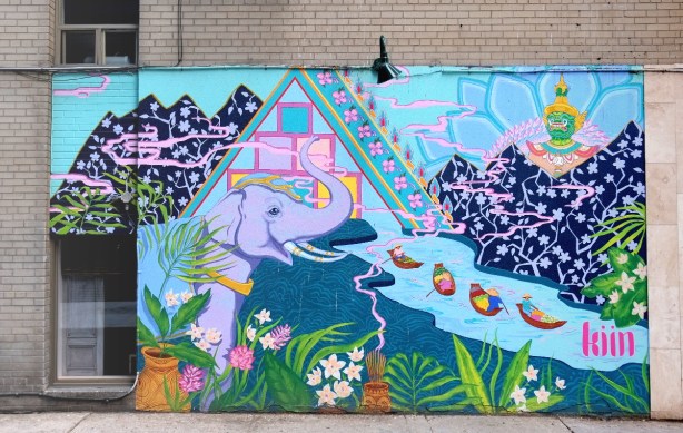 mural on the side of Kiin restaurant, a purple elephant standing beside a river with four boats, flowers growing beside the river. 