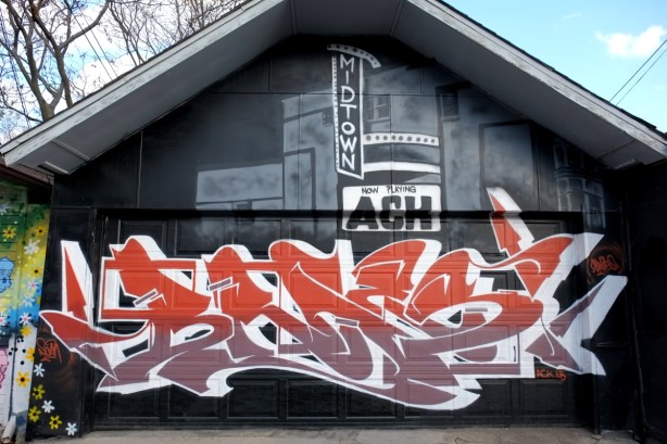 mural on a garage, red and light brown text on the botto, grey tones picture of midtown cinema on the top part