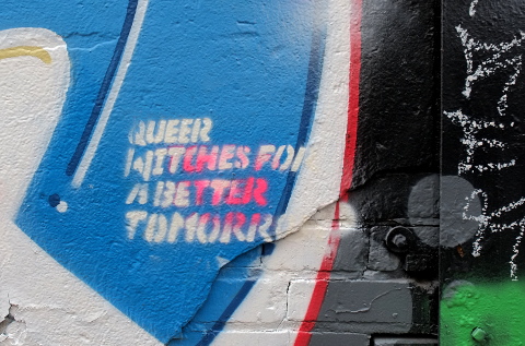 graffiti words stencilled on a wall that say Queer witches for a better tomorrow