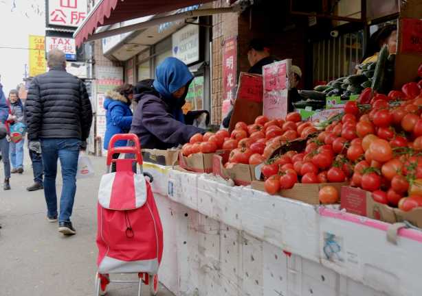 a woman is buying tomatos from a vendor with a large table of tomatoes outside a Chinese grocery store on Spadina, in CHinatown. 
