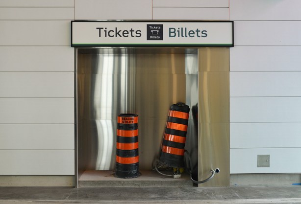 unfinished part of the subway station, indent in wall with sign tickets billets but the niche is empty except for two large black and orange striped construction cones