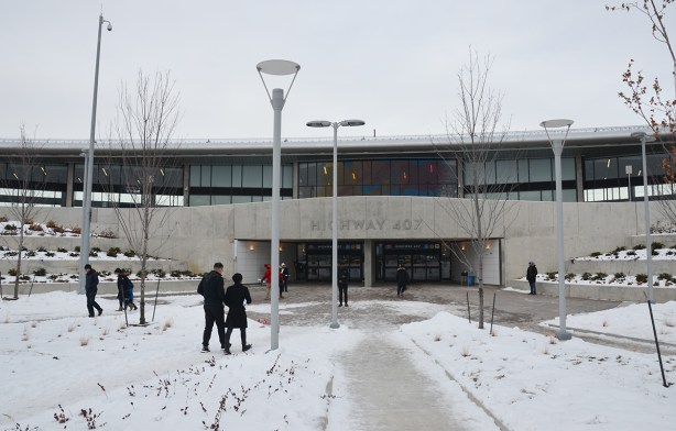 people walking towards the entrance to HUghway 407 TYSSE station, a low concrete and glass building.