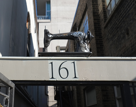an old SInger sewing machine sits on a beam that crosses a small alley bewteen two buildings, it's about 8 feet above the street level 