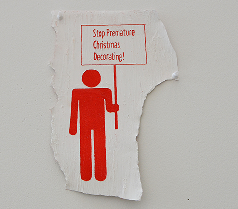 red and white paintings of demonstraion signs being held by stick figure men part of an art exhibit at fleck conservatory - sign says stop premature Christmas decorations
