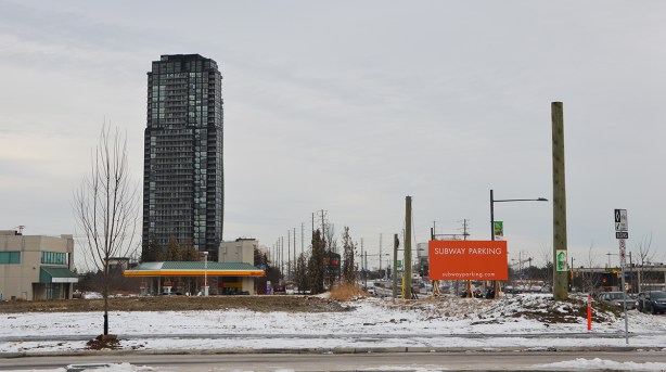 suburbia - empty field with orange sign that says Subway parking. one tall building, a gas station, a street,