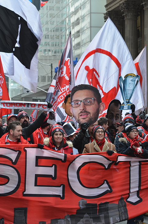 Toronto FC parade, people dressed in red and white, a group holding a banner as they walk