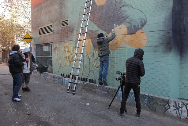 one man with video camera filming another man painting a mural in Graffiti Alley