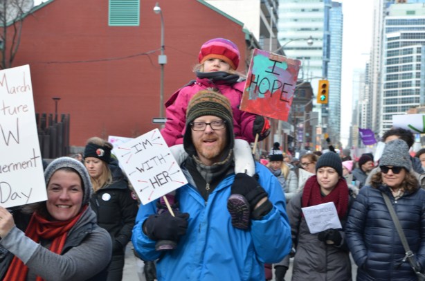 little girl on father's shoulders in Toronto womens march on Bay street, holding sign that says I hope
