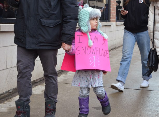 Womens march, protest parade - a girl walking with her father, she has a pink sign that says I am a snowflake 