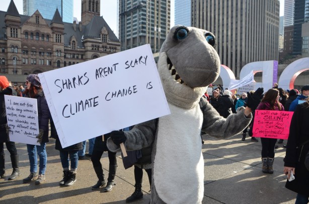 person in shark costume holding a sign that says sharks aren't scary, climate change is. 