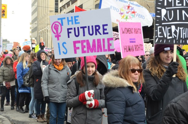 group walking in a protest march, the future is female is one of the signs being carried, walking on Dundas St