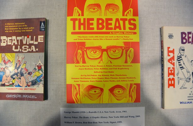 display in a glass top case, three books by Alan Ginsberg, the one in the middle has a yellow cover and is The Beats