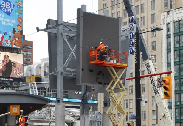 two men on a lift are working on a new elevated sign at Dundas square 