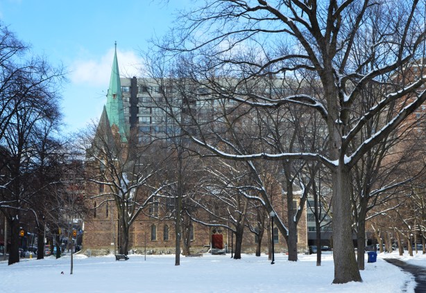park, in winter, with large mature trees, in the background is Grace Church, brick building with green roofed steeple 