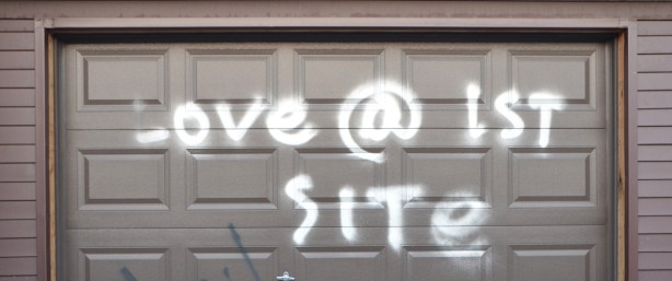 dark brown garage door,metal, with white spray paint words that say love @ first site 