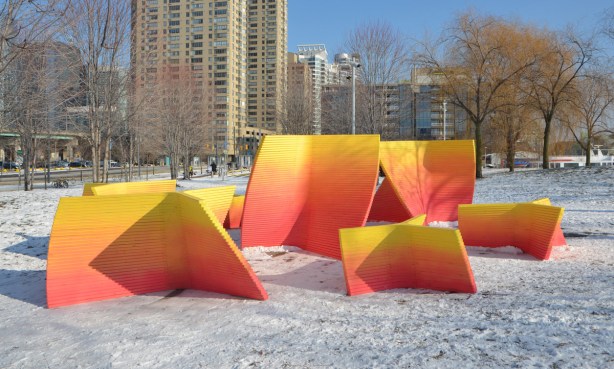 6 or 7 large wooden forms in convex and concave shapes in a snow covered park with highrises in the background. An art installation that is part of Ice Breakers 2018 on Toronto waterfront. 